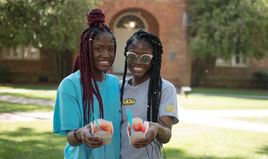 Two students smile and hold their snow cones out towards the camera.